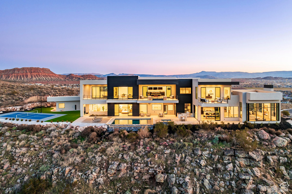 Back house at dusk with a balcony, a patio area, and a mountain view