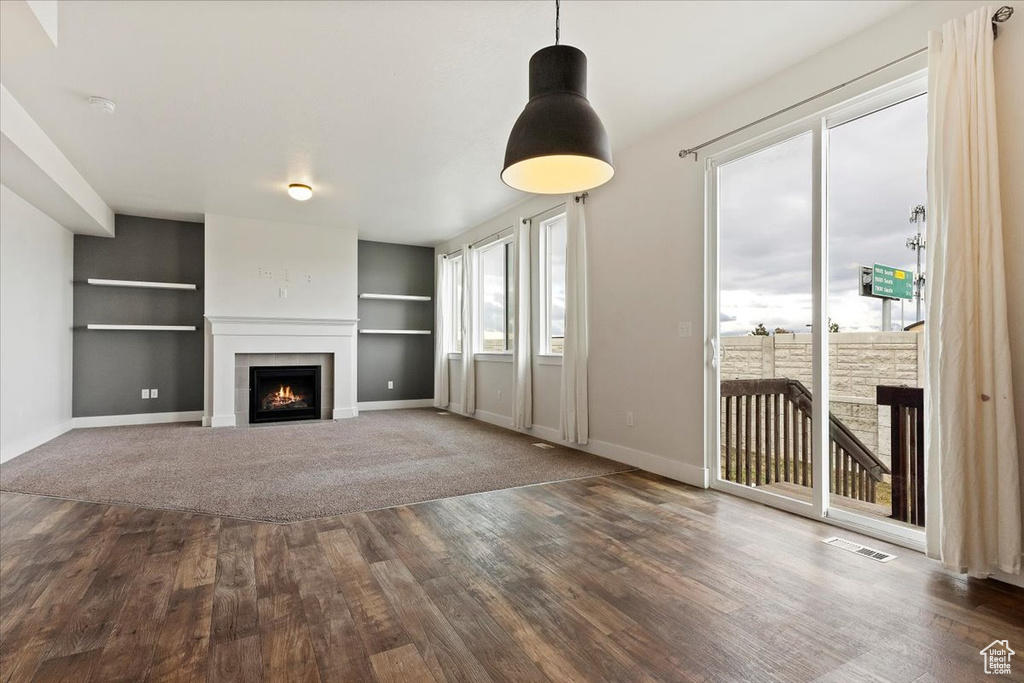 Unfurnished living room featuring a tiled fireplace, dark wood-type flooring, and built in features