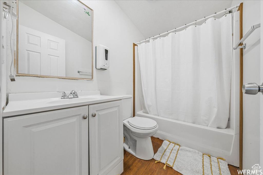 Full bathroom featuring shower / bathtub combination with curtain, lofted ceiling, vanity, hardwood / wood-style flooring, and toilet