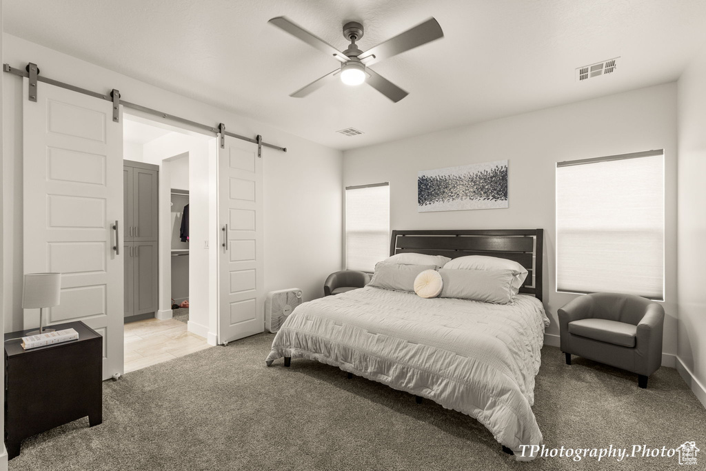 Bedroom featuring a barn door, carpet floors, ceiling fan, and a walk in closet