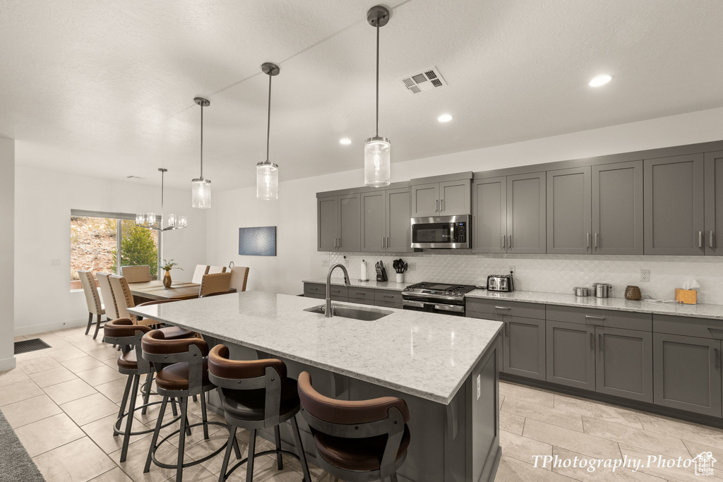 Kitchen featuring light stone counters, a kitchen island with sink, sink, a notable chandelier, and appliances with stainless steel finishes