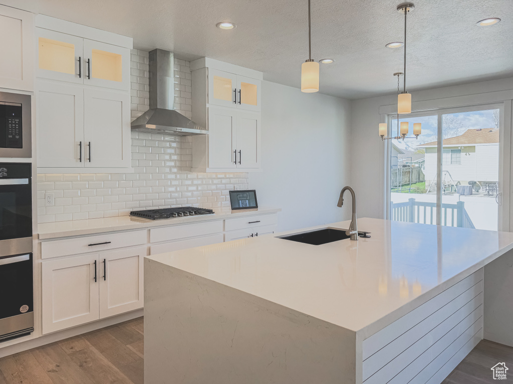 Kitchen featuring backsplash, hanging light fixtures, light hardwood / wood-style floors, and wall chimney exhaust hood