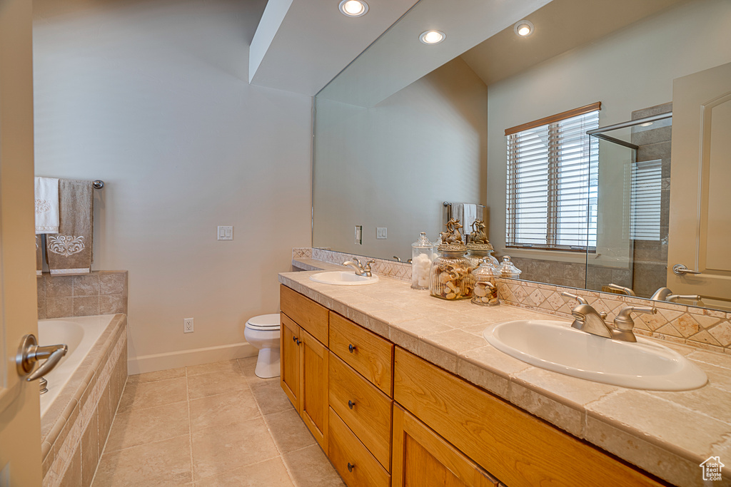 Bathroom featuring toilet, tiled tub, dual bowl vanity, and tile flooring