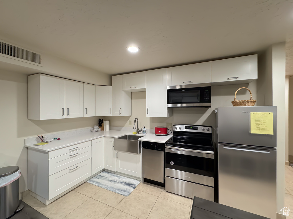 Kitchen with white cabinets, appliances with stainless steel finishes, light tile flooring, and sink