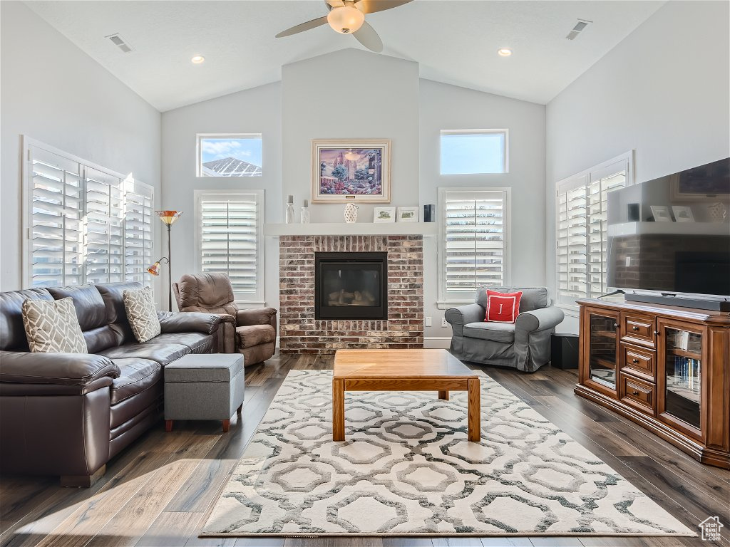 Living room featuring a fireplace, high vaulted ceiling, dark wood-type flooring, and ceiling fan