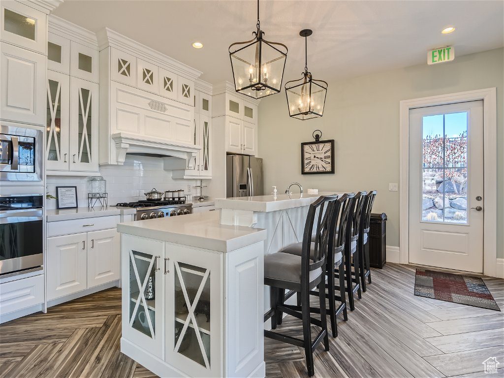 Kitchen featuring dark parquet flooring, a breakfast bar, a notable chandelier, an island with sink, and appliances with stainless steel finishes