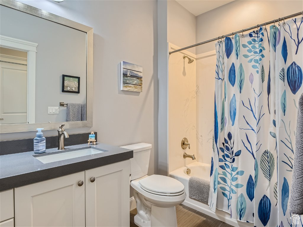Full bathroom with hardwood / wood-style flooring, shower / bath combo, oversized vanity, and toilet