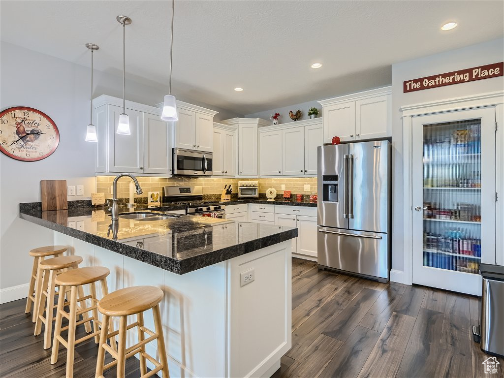 Kitchen with dark hardwood / wood-style flooring, stainless steel appliances, white cabinets, tasteful backsplash, and hanging light fixtures