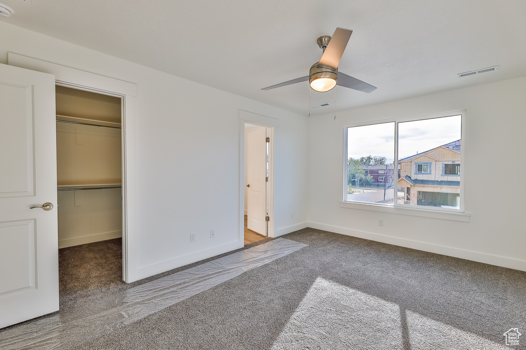 Unfurnished bedroom featuring dark colored carpet, a spacious closet, ceiling fan, and a closet