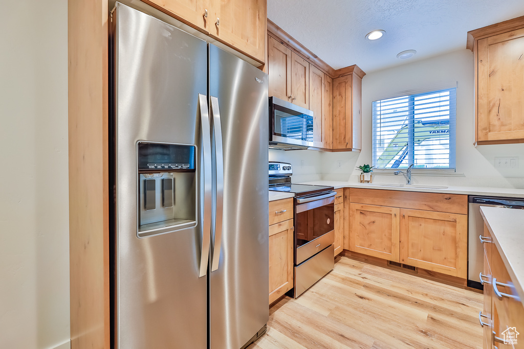 Kitchen with appliances with stainless steel finishes, light hardwood / wood-style floors, and sink