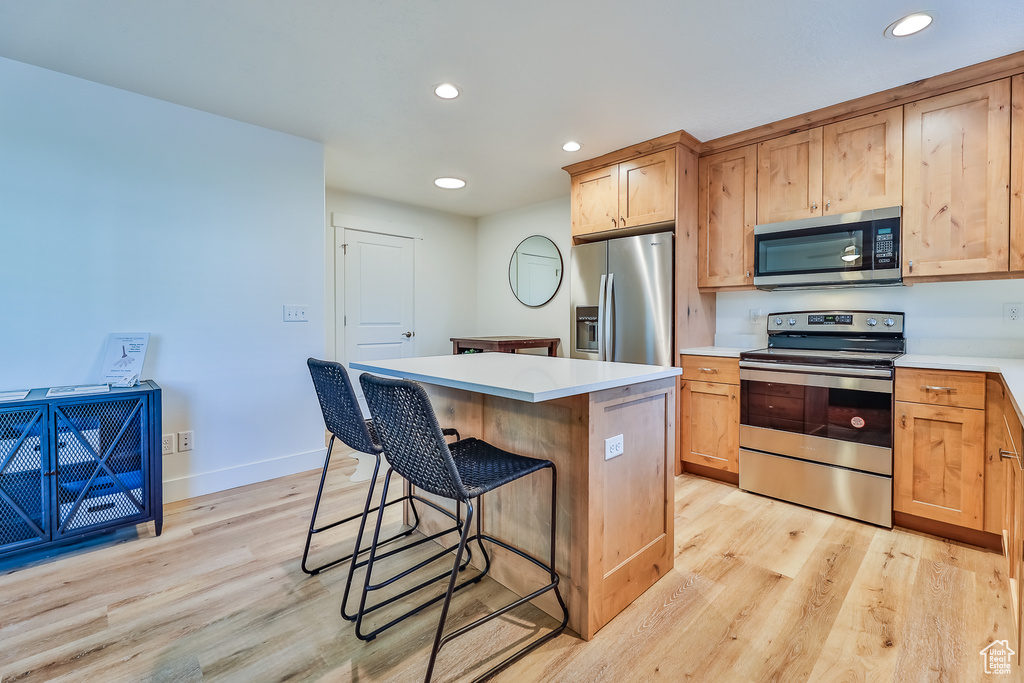 Kitchen with a kitchen island, appliances with stainless steel finishes, light hardwood / wood-style flooring, and a kitchen bar
