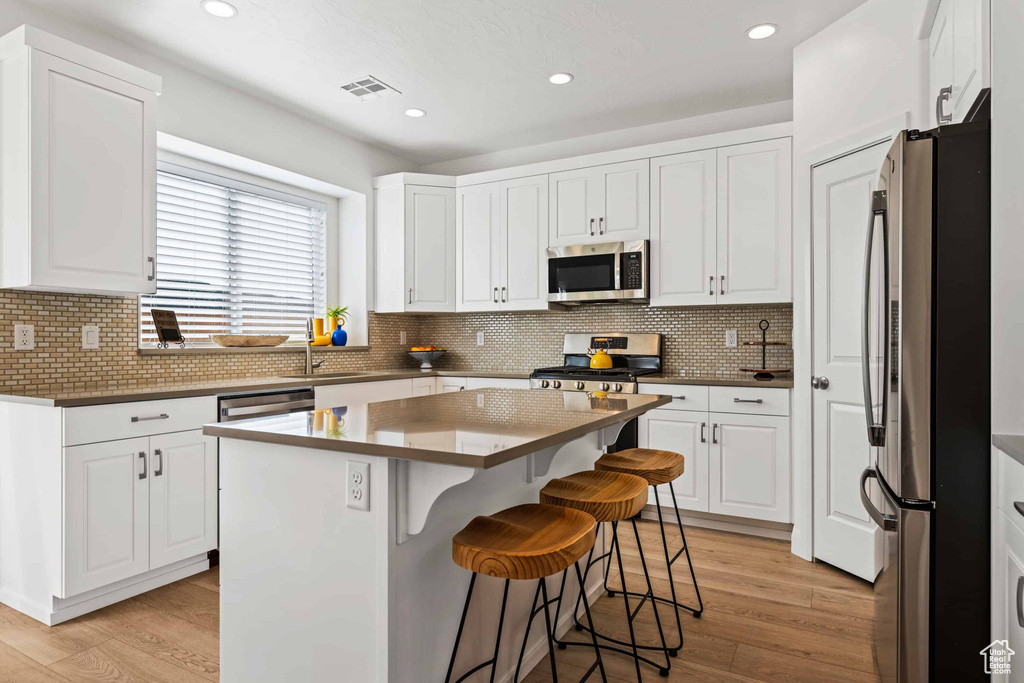 Kitchen with a kitchen island, appliances with stainless steel finishes, a kitchen breakfast bar, and white cabinetry