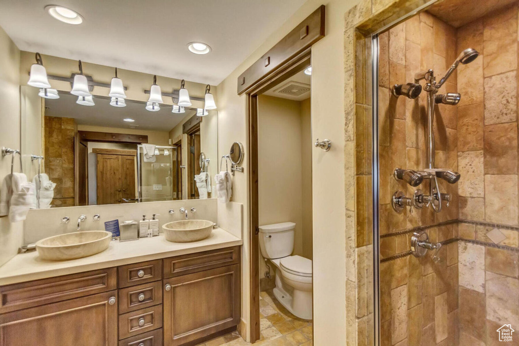 Bathroom with vanity with extensive cabinet space, walk in shower, double sink, toilet, and tile flooring