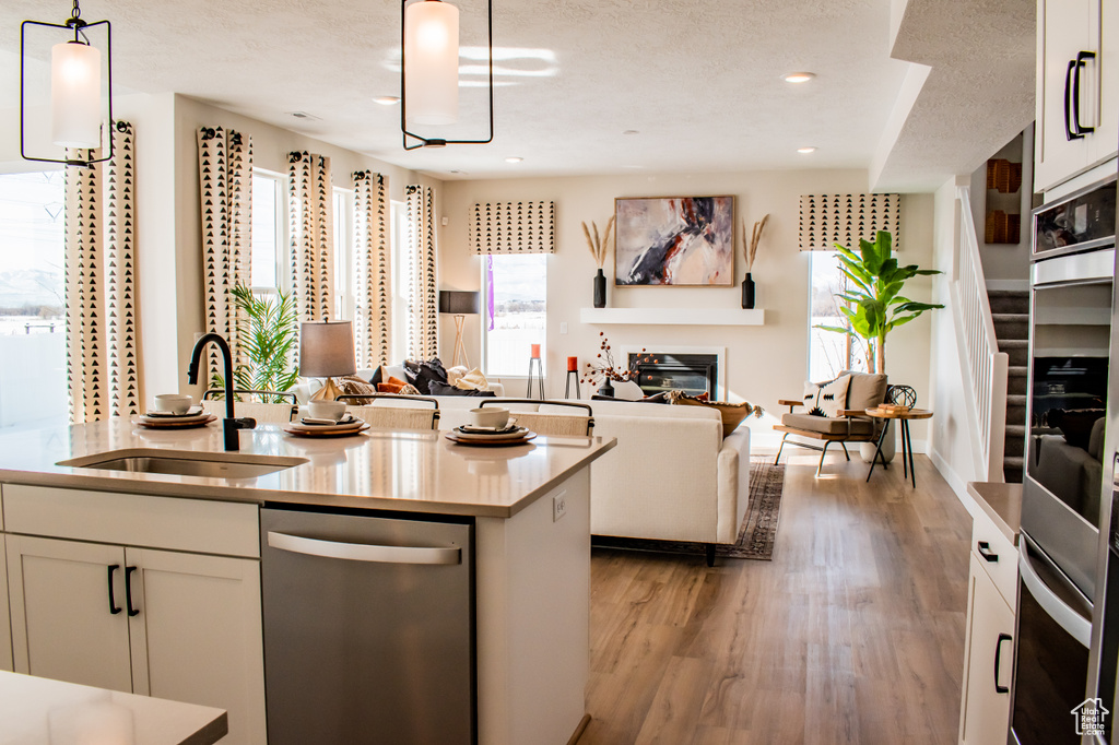 Kitchen featuring light wood-type flooring, white cabinets, sink, stainless steel appliances, and pendant lighting