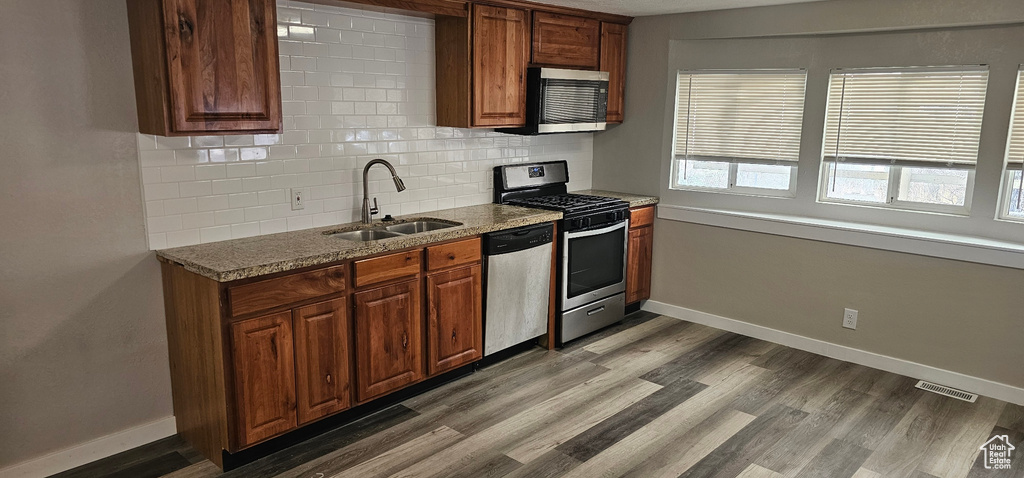Kitchen featuring tasteful backsplash, sink, dark stone countertops, appliances with stainless steel finishes, and light hardwood / wood-style floors