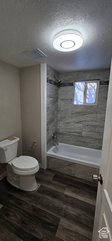 Bathroom with tiled shower / bath combo, a textured ceiling, and toilet