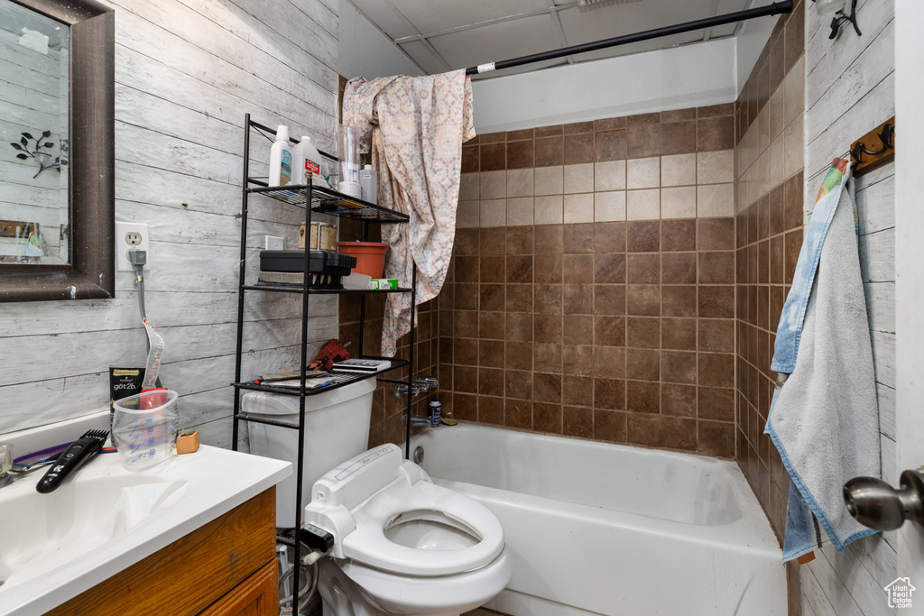 Full bathroom with wooden walls, vanity, tiled shower / bath combo, and toilet