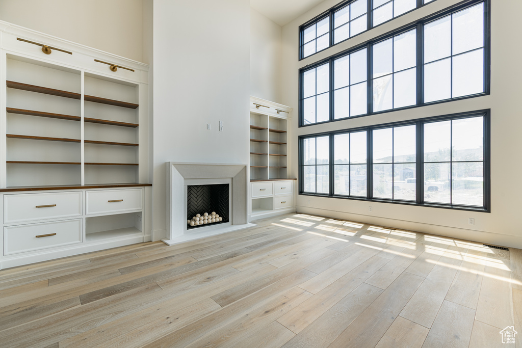 Unfurnished living room featuring light hardwood / wood-style flooring, built in shelves, and a high ceiling