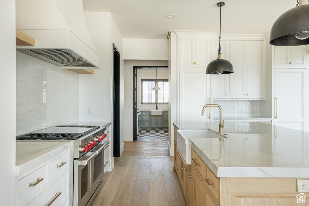Kitchen featuring light wood-type flooring, white cabinets, tasteful backsplash, premium range hood, and double oven range