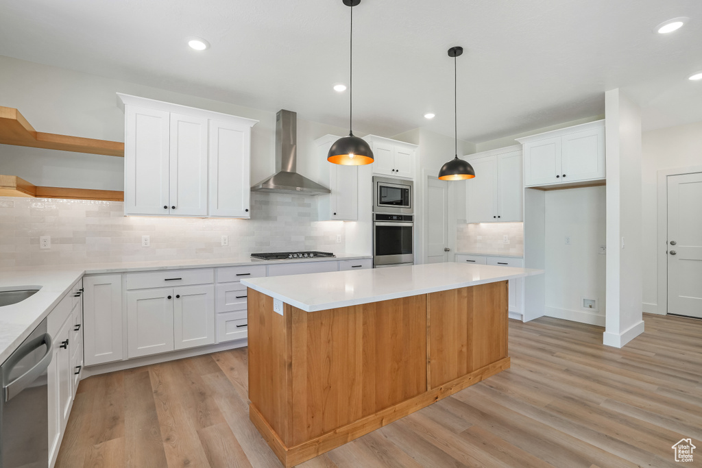 Kitchen with light hardwood / wood-style floors, white cabinets, tasteful backsplash, appliances with stainless steel finishes, and wall chimney range hood