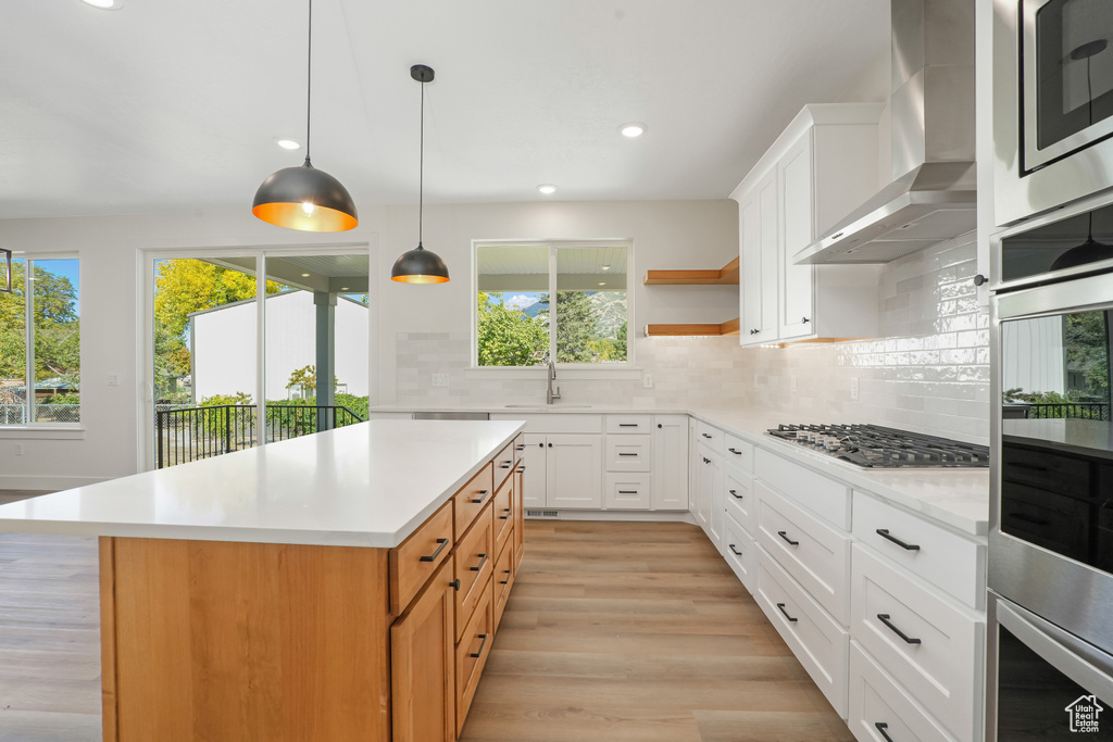 Kitchen with white cabinets, a kitchen island, backsplash, and wall chimney exhaust hood