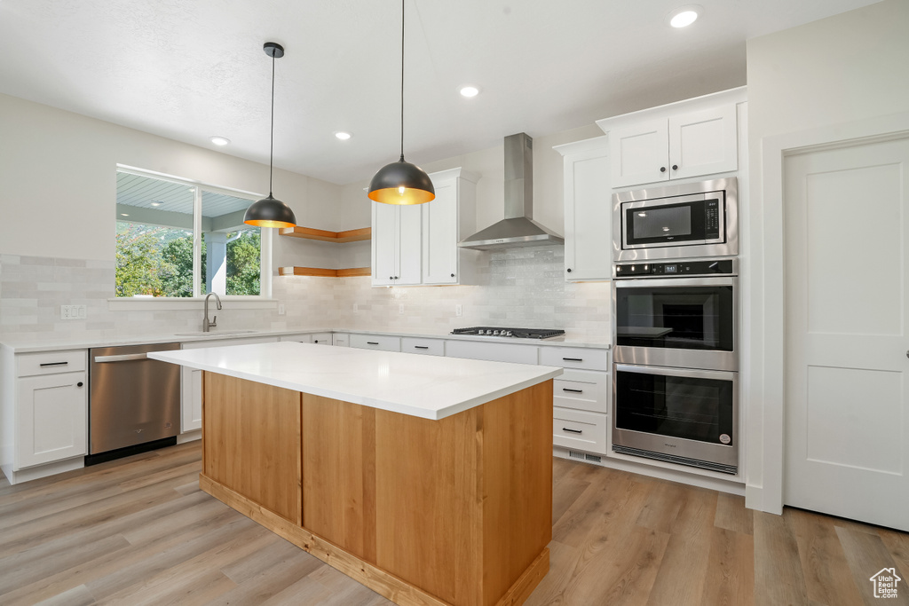Kitchen with light hardwood / wood-style floors, a center island, appliances with stainless steel finishes, and wall chimney range hood