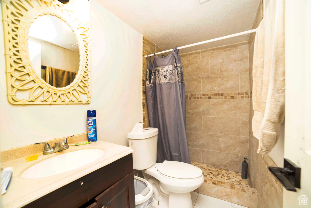 Bathroom with a textured ceiling, toilet, a shower with curtain, large vanity, and tile flooring
