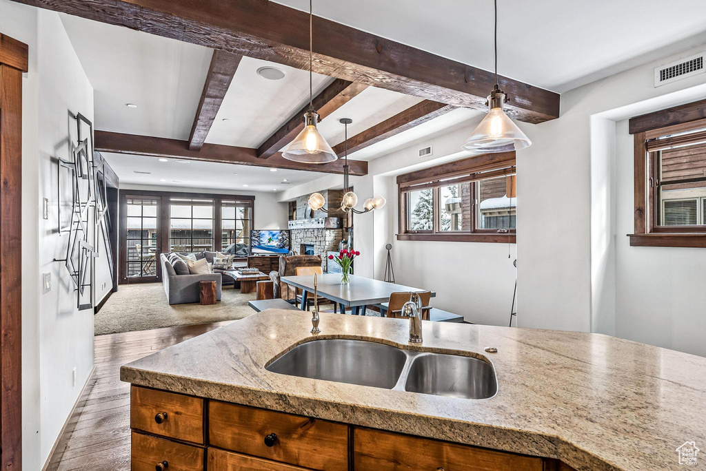 Kitchen with hanging light fixtures, beamed ceiling, light wood-type flooring, and light stone counters