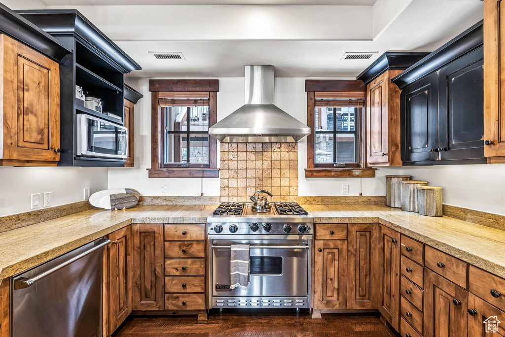 Kitchen featuring appliances with stainless steel finishes, wall chimney range hood, a healthy amount of sunlight, and dark wood-type flooring