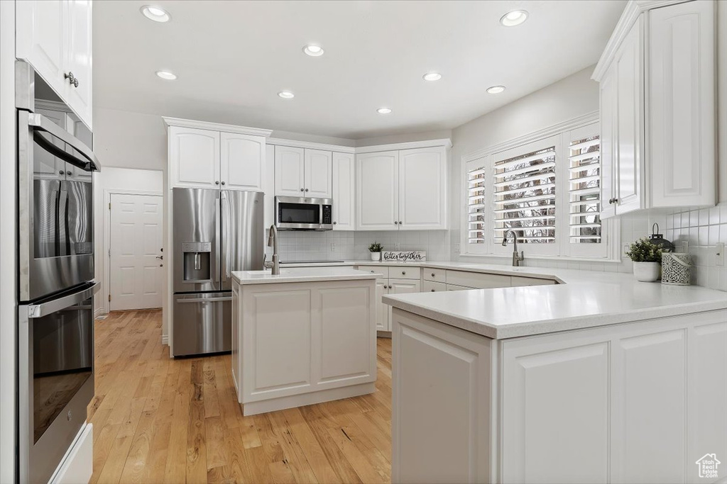 Kitchen featuring light wood-type flooring, appliances with stainless steel finishes, tasteful backsplash, and white cabinets