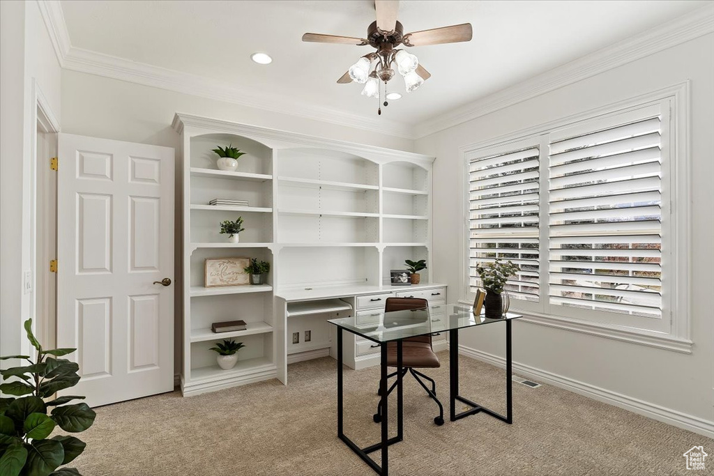 Office space with crown molding, ceiling fan, built in desk, and light carpet