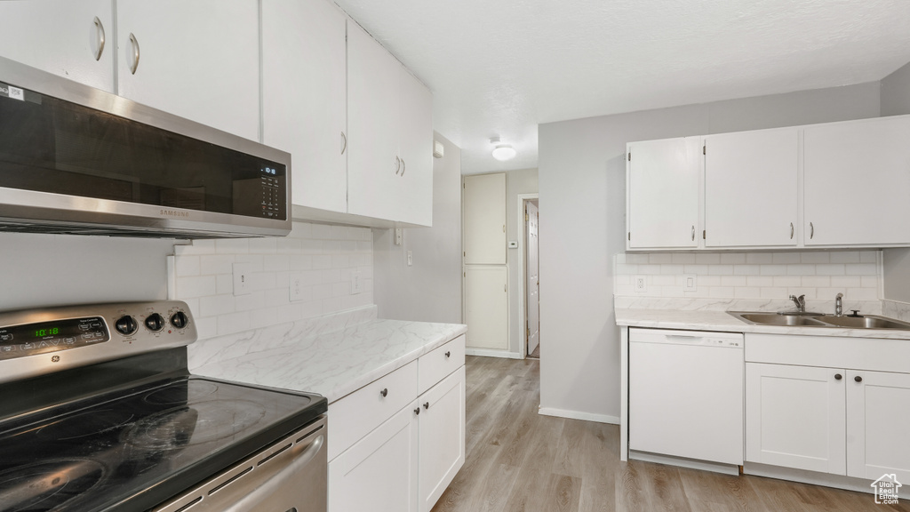 Kitchen with light hardwood / wood-style flooring, stainless steel appliances, backsplash, and white cabinets