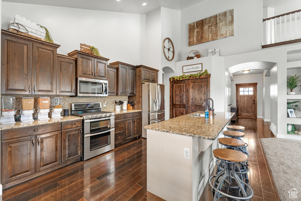 Kitchen with backsplash, a kitchen breakfast bar, dark hardwood / wood-style flooring, sink, and appliances with stainless steel finishes