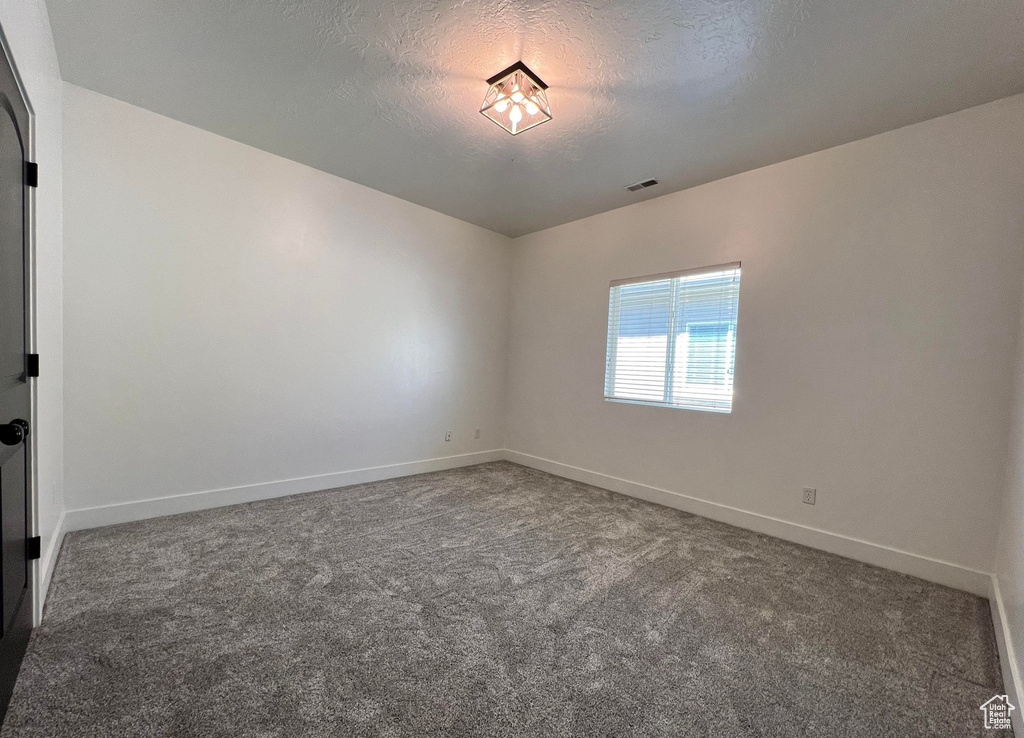 Empty room featuring dark colored carpet and a textured ceiling