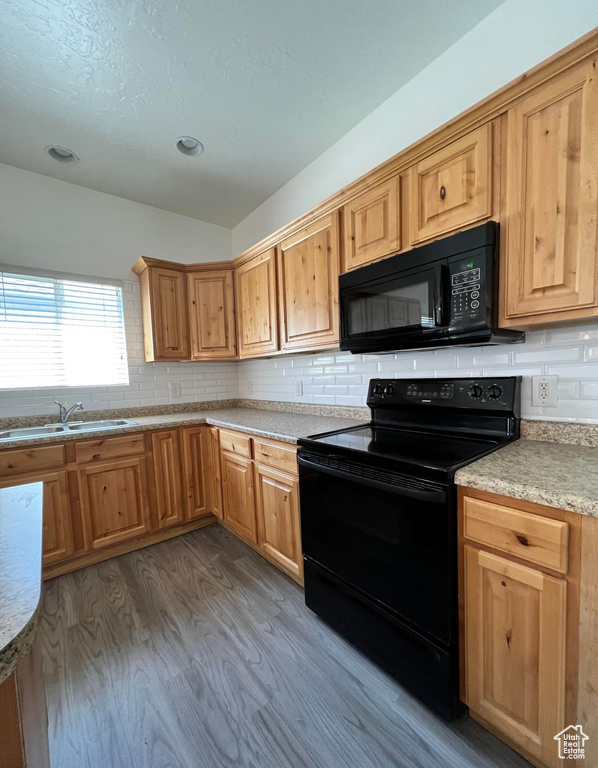 Kitchen featuring tasteful backsplash, hardwood / wood-style floors, sink, and black appliances