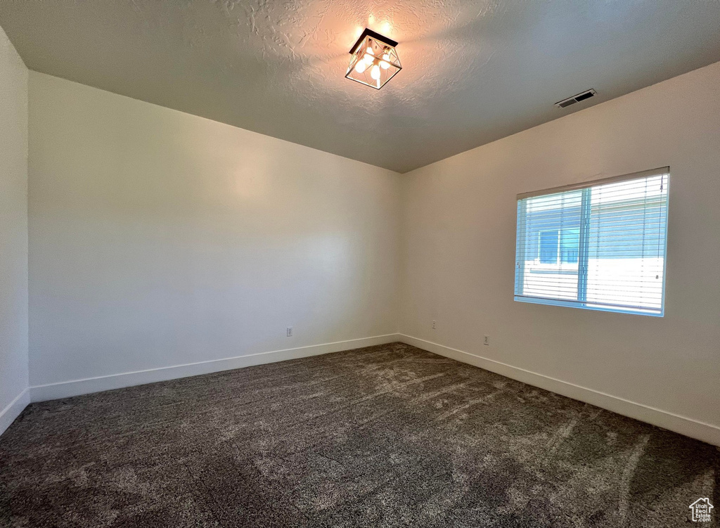 Empty room with dark carpet and a textured ceiling