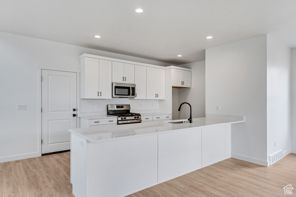 Kitchen with white cabinetry, light hardwood / wood-style floors, sink, and appliances with stainless steel finishes