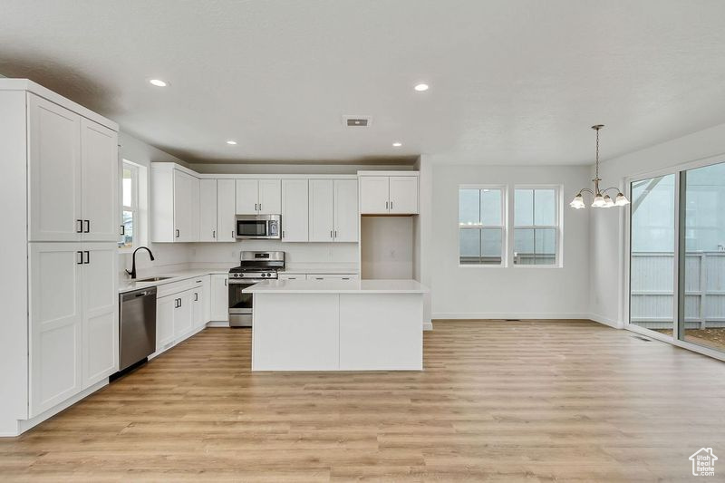 Kitchen with light wood-type flooring, a notable chandelier, white cabinetry, appliances with stainless steel finishes, and decorative light fixtures