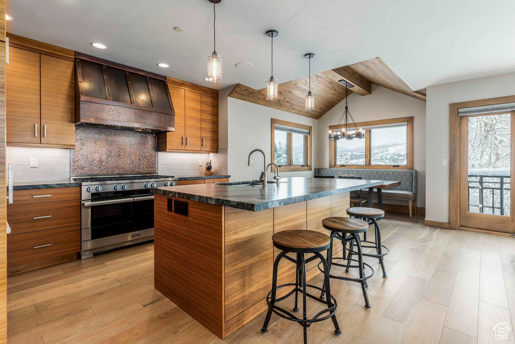 Kitchen with custom exhaust hood, double oven range, sink, light wood-type flooring, and a kitchen island with sink
