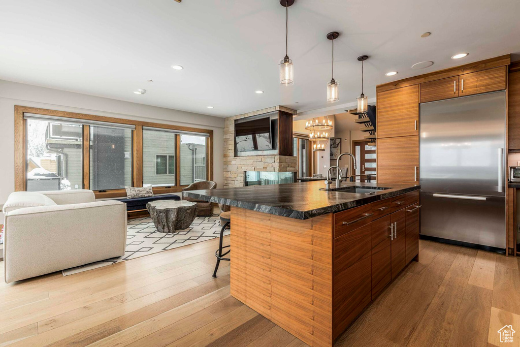 Kitchen with a kitchen bar, light hardwood / wood-style floors, built in refrigerator, hanging light fixtures, and an island with sink