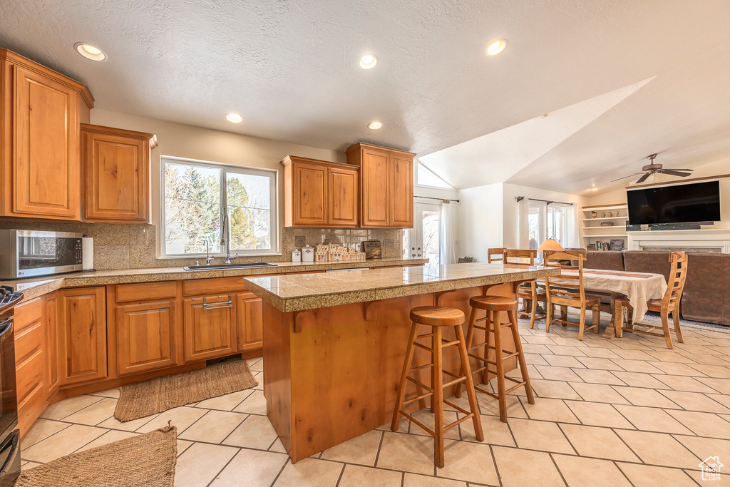 Kitchen featuring a kitchen island, a breakfast bar, vaulted ceiling, light tile floors, and ceiling fan