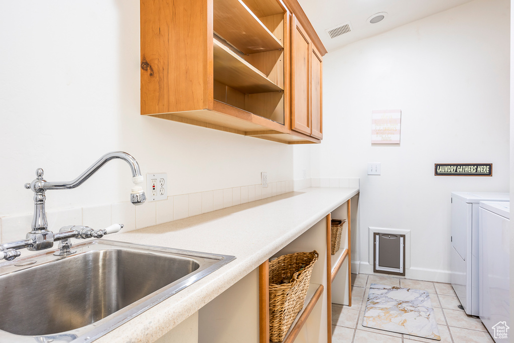 Laundry room featuring washing machine and clothes dryer, sink, light tile flooring, and cabinets