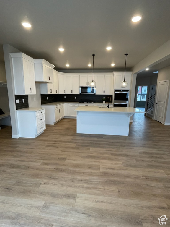 Kitchen with light hardwood / wood-style flooring, a kitchen island with sink, white cabinetry, stainless steel appliances, and pendant lighting