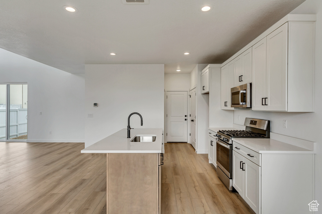 Kitchen with light wood-type flooring, white cabinets, sink, an island with sink, and stainless steel appliances