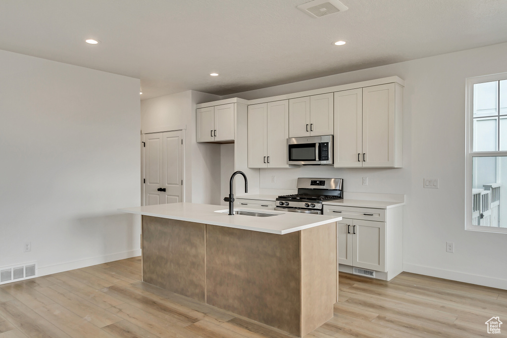 Kitchen featuring white cabinets, light hardwood / wood-style flooring, appliances with stainless steel finishes, and a center island with sink