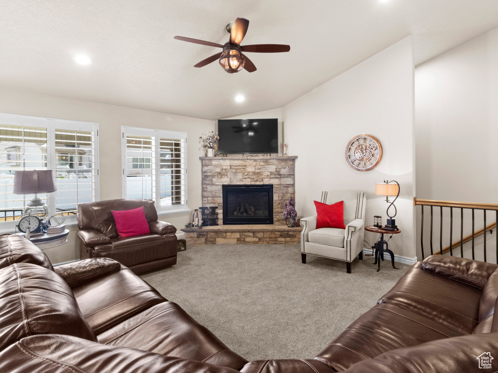 Living room with ceiling fan, light carpet, vaulted ceiling, and a stone fireplace
