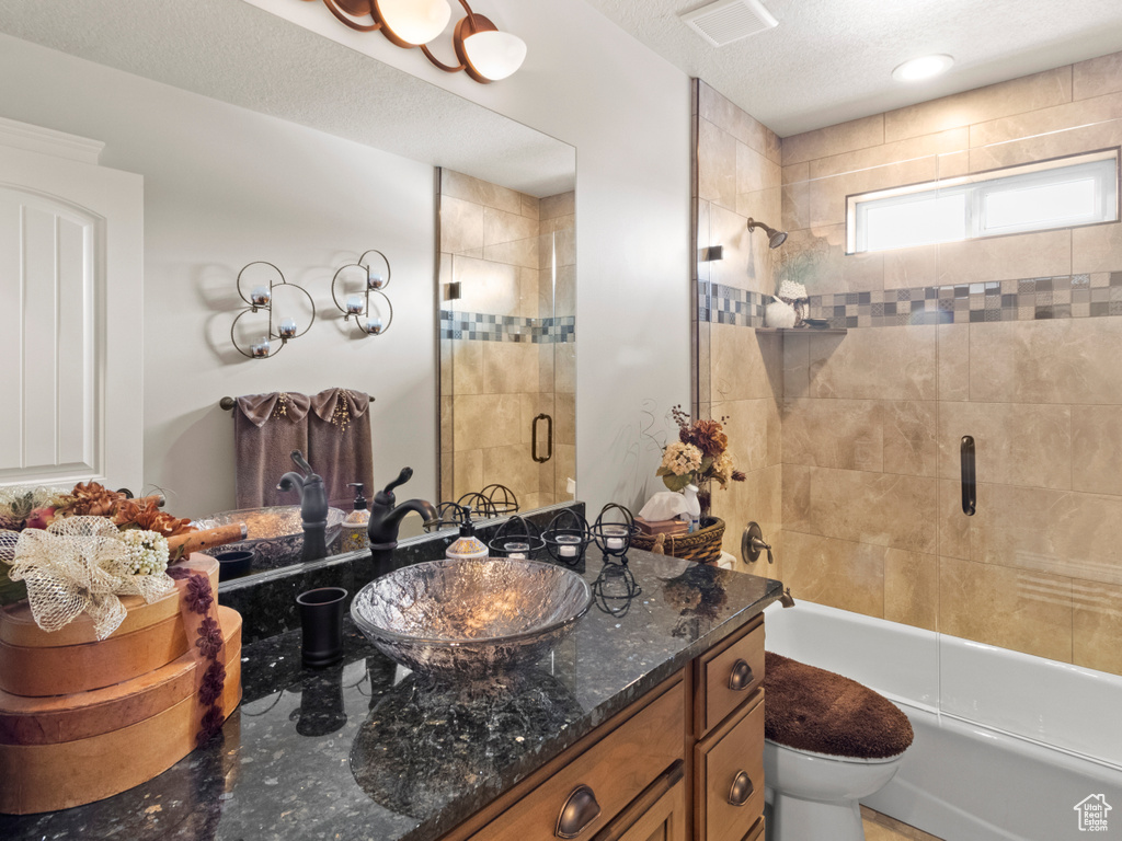 Full bathroom with vanity, toilet, a textured ceiling, and combined bath / shower with glass door