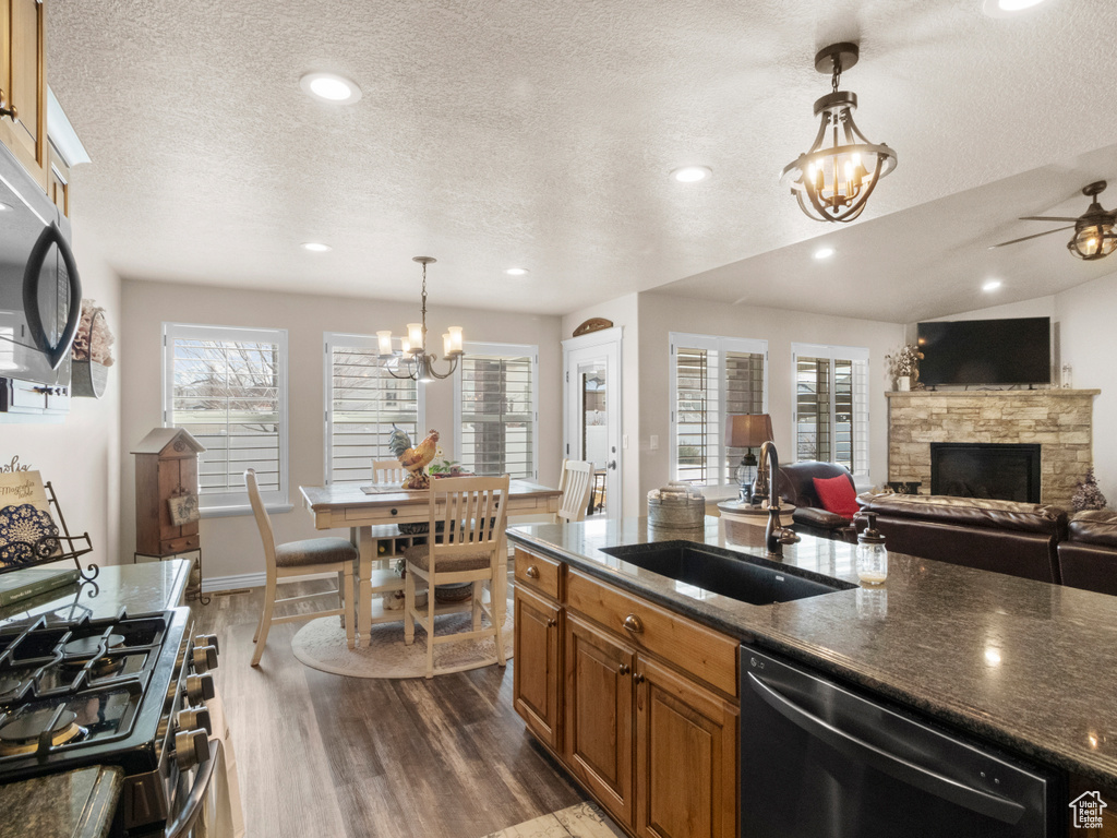 Kitchen with a fireplace, dark wood-type flooring, ceiling fan with notable chandelier, sink, and appliances with stainless steel finishes