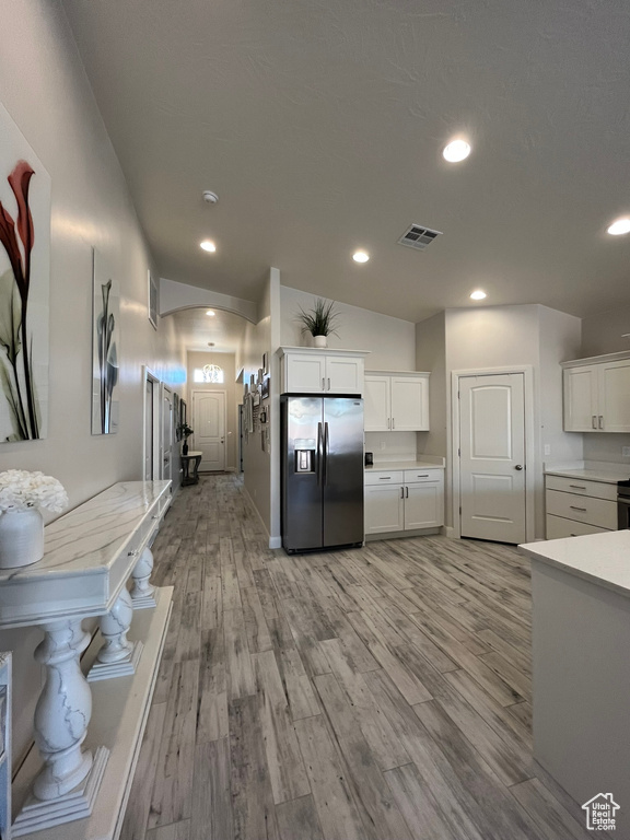Kitchen featuring white cabinets, light hardwood / wood-style floors, stainless steel fridge with ice dispenser, and vaulted ceiling