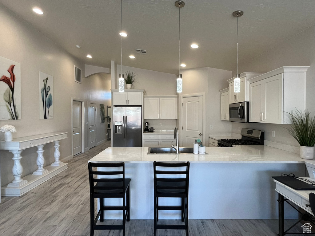 Kitchen featuring stainless steel appliances, white cabinets, hanging light fixtures, light hardwood / wood-style flooring, and sink